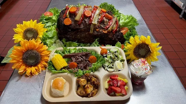 A bison roast served with a salad, roll and fruit.