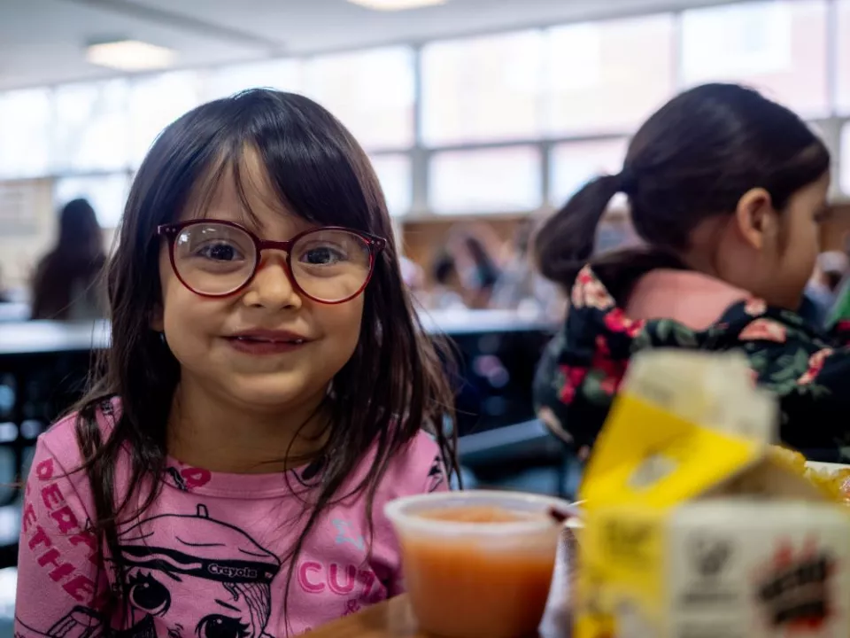 A young elementary student sits at a cafeteria table during lunch in front of her tray.