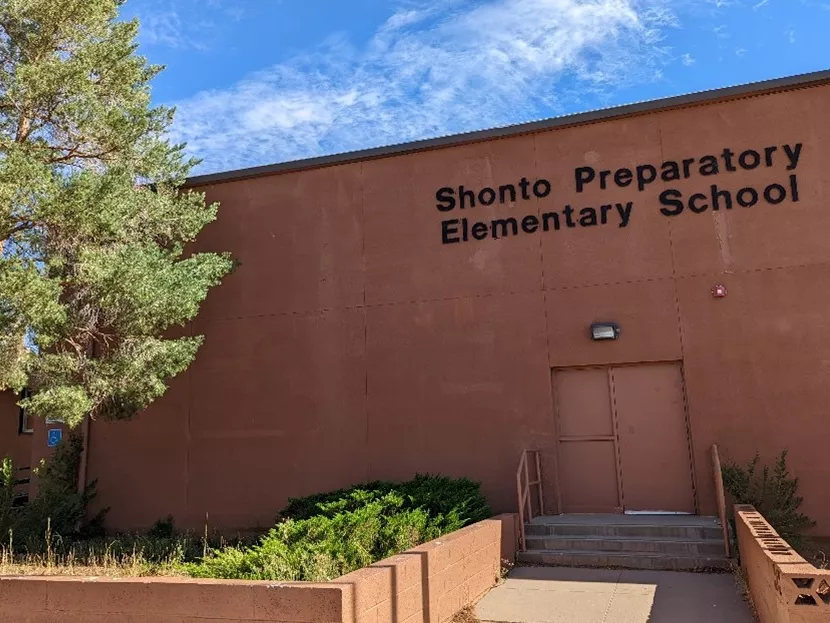 A rust red school building with Shonto Preparatory Elementary School written in black letters and a tree to the left.
