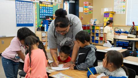 A teacher is leaning over a student's desk to help them with an assignment.