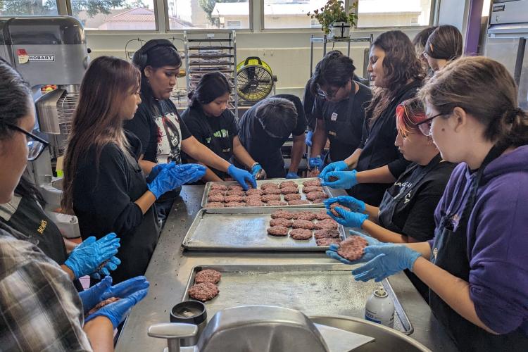 Students gather around a table to help prepare food for lunch.