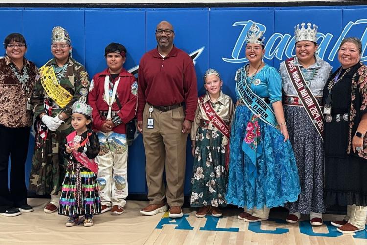 A line of students and community members named Baca Community School royalty post for a picture in a gymnasium.