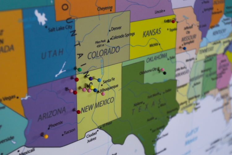 A map of the United States on a corkboard with pins stuck in it.