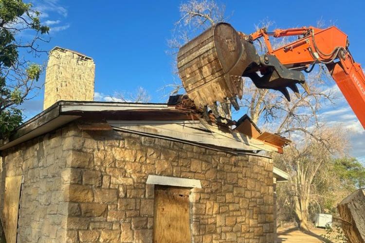 A large piece of construction equipment digs into a stone building to demolish it.
