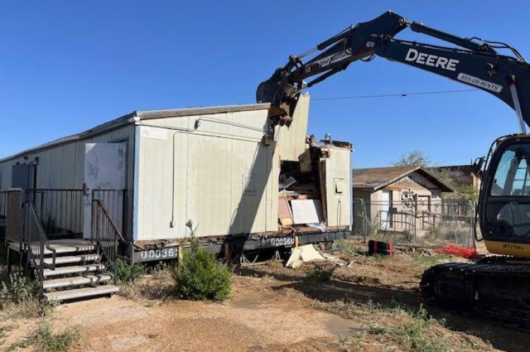 A construction crane demolishes a portable building.