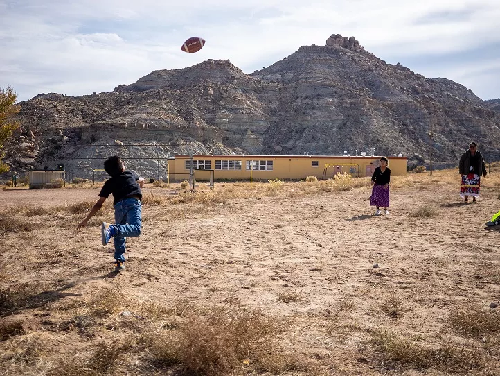 A small group of kids throw a football back and forth in front of a school.