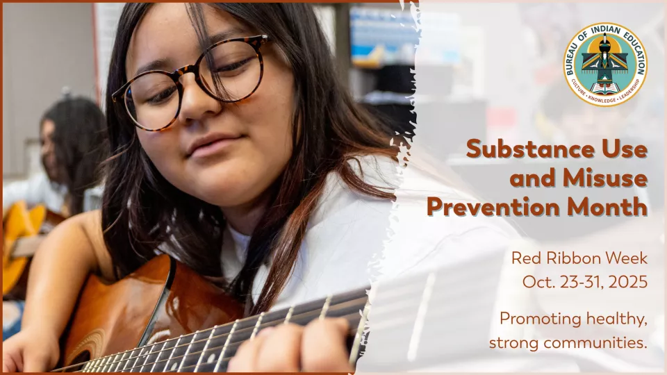 A student with dark, round glasses and long, brown hair plays the guitar.