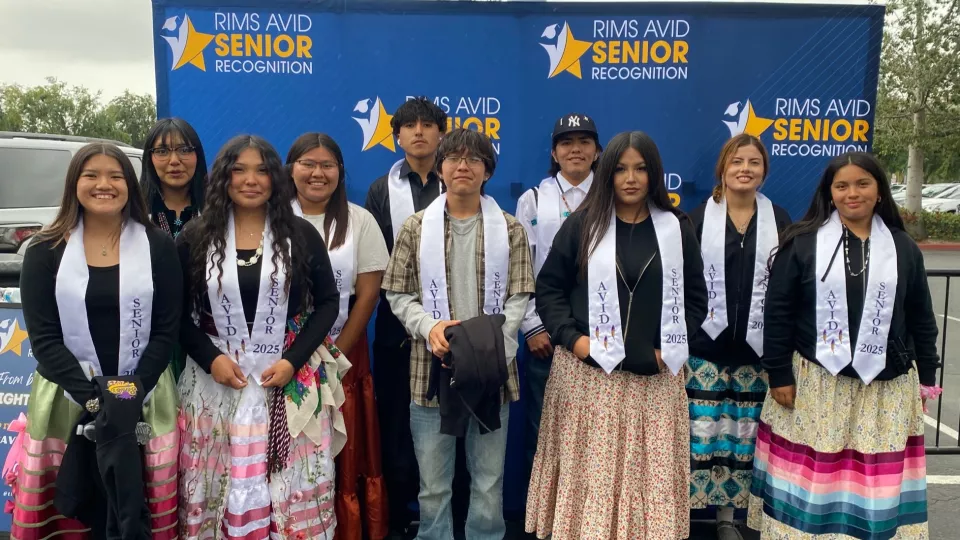 Ten high schoolers stand for a group photo in front of a blue backdrop that says "RIMS AVID Senior Recognition."