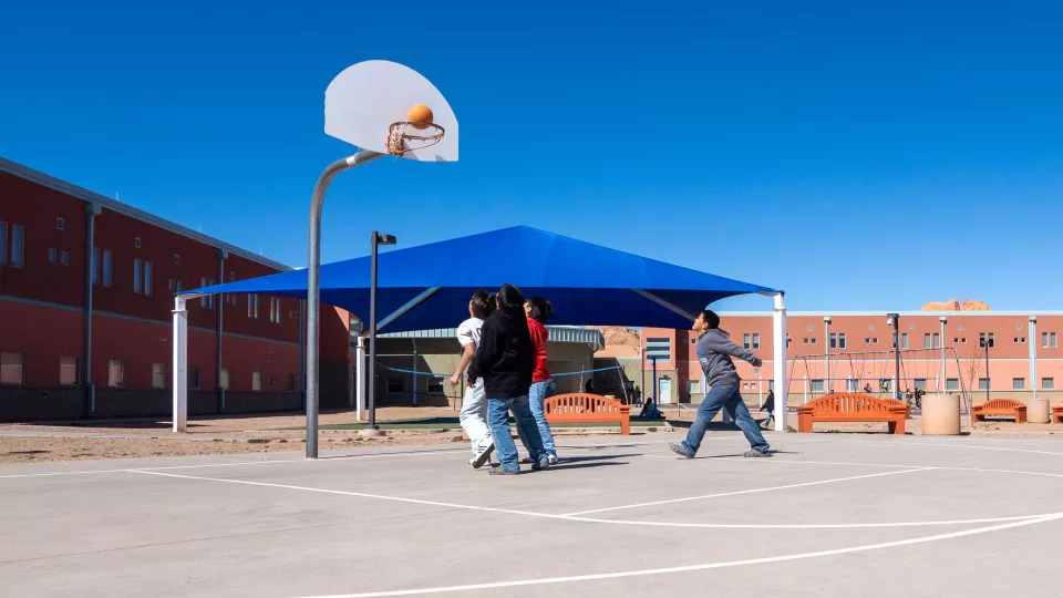 A group of students plays 2-on-2 basketball on a playground court.
