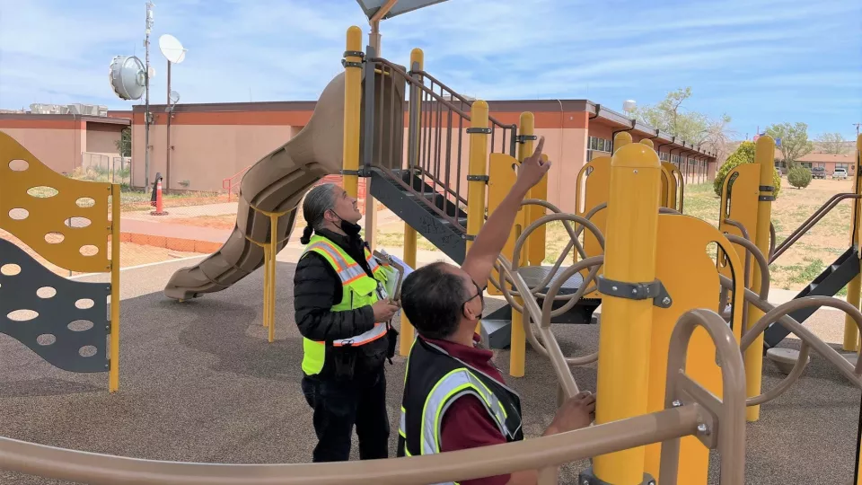 Two Branch of Safety Management inspectors evaluate a playground at an elementary school.