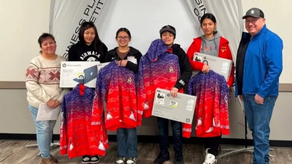 A group of four students poses with colorful jackets and other prizes they won alongside their two mentors.