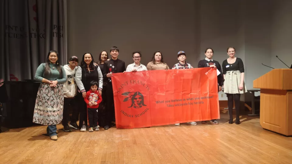 A group of students stands in a line holding up a red banner that says, "What you believe is what you achieve."