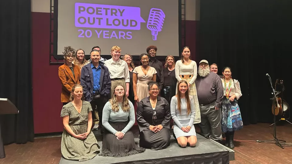 A group of high schoolers and teachers pose for a photo on a stage.