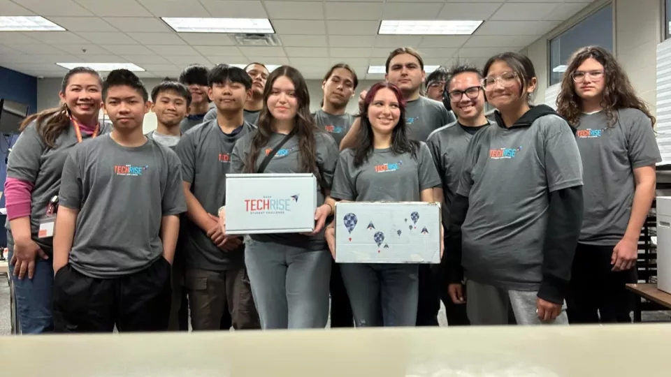 A group of students dressed in grey team t-shirts hold up their certificates.