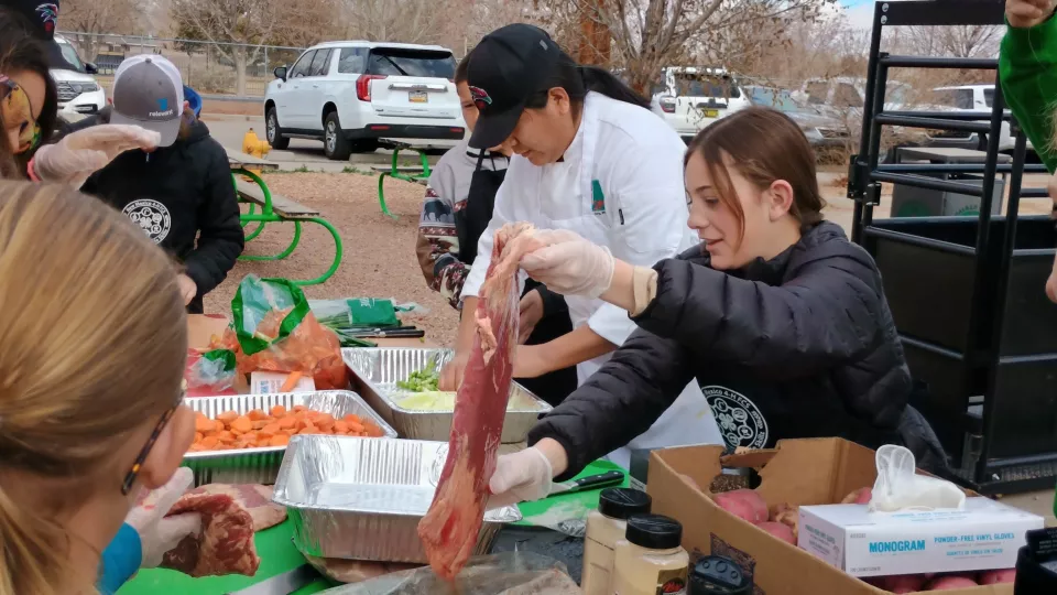 A chef in a white coat and a young student stand at a table and prepare food for cooking.