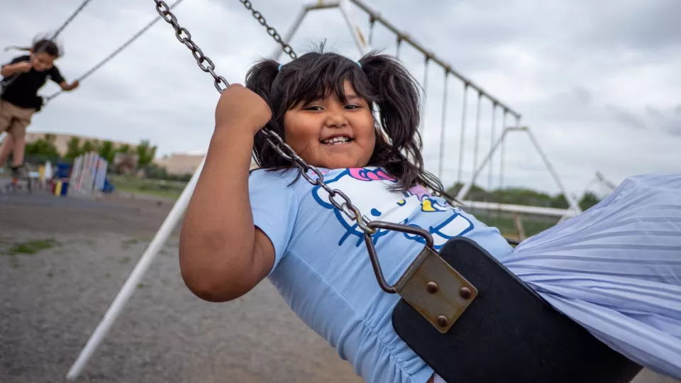 A girl smiles while swinging on a playground swing set.