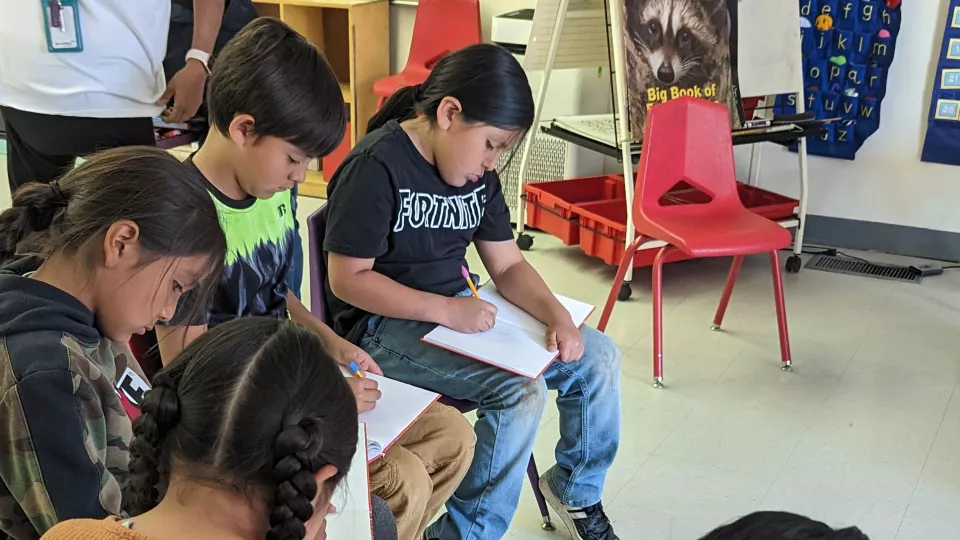 A group of students sit in a circle and write in notebooks.