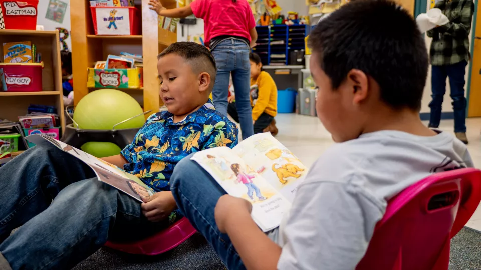 Two students sit and read on the floor in a classroom.