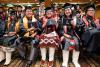 A group of students sit at a graduation ceremony in their caps and gowns, holding up either diploma casings.