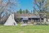 A teepee sits on a field of grass in front of a library surrounded by trees.